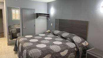 This image shows a modern bedroom with a neatly made bed featuring a patterned bedspread, gray walls, and minimal furnishings.