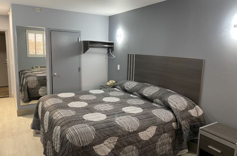 This image shows a modern bedroom with a neatly made bed featuring a patterned bedspread, gray walls, and minimal furnishings.